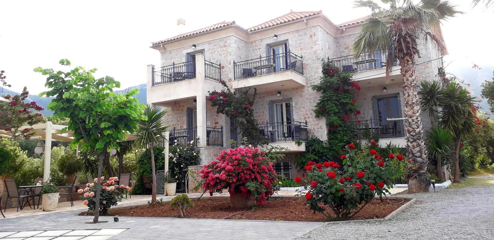 Το πέτρινο κτίριο με τα μπαλκόνια και τον κήπο με τριανταφυλλιές